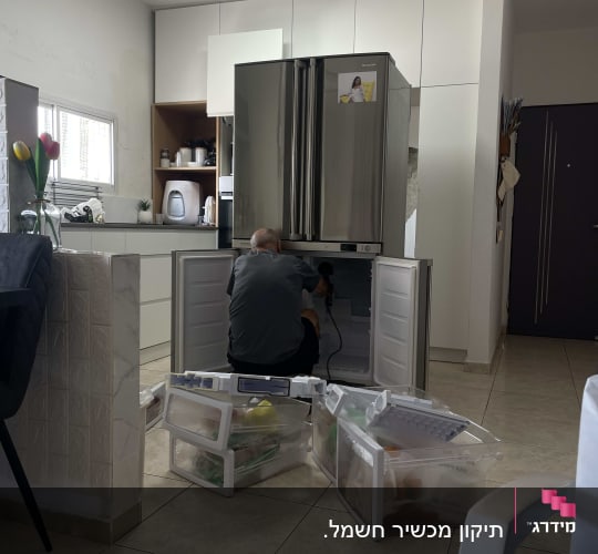 אדם מתקן מקרר עם מגירות פתוחות על הרצפה